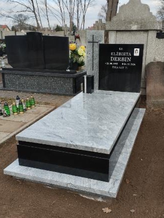 Dwukolorowy nagrobek na cmentarzu Kampinos: jasnoszary kamień z ciemnymi żyłkami i czarne elementy. Widoczny napis z imieniem i nazwiskiem oraz datami urodzenia i śmierci. W tle inne nagrobki...