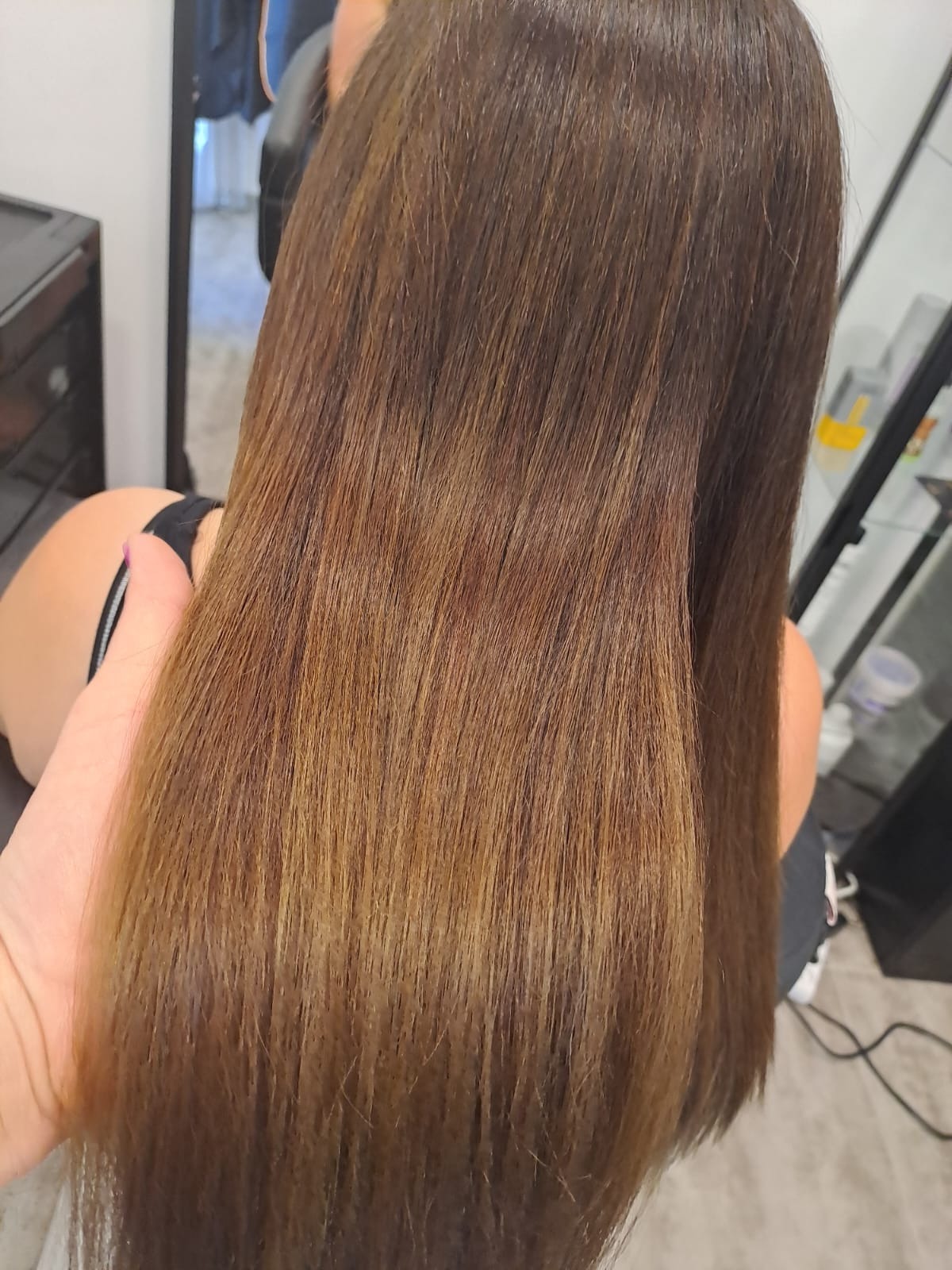 Proste, brązowe włosy z delikatnym ombre, widoczne od tyłu w salonie fryzjerskim, trzymane w dłoni.