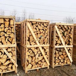 WBO Tartak - Rzęd rzędów drewnianych skrzyń wypełnionych pociętym drewnem opałowym, ustawionych na ziemi, z widocznymi śladami opon w tle i nagimi drzewami na horyzoncie.