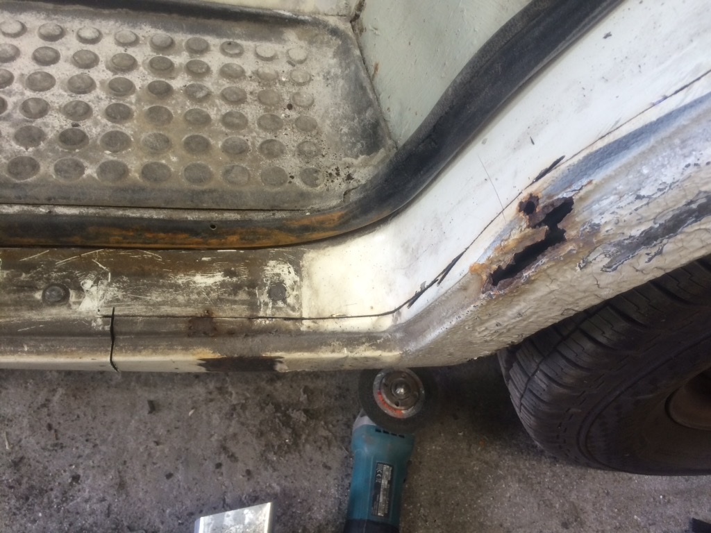 Zardzewiały próg samochodu z widocznymi dziurami i szlifierką kątową przygotowaną do pracy, widoczny bieżnik opony