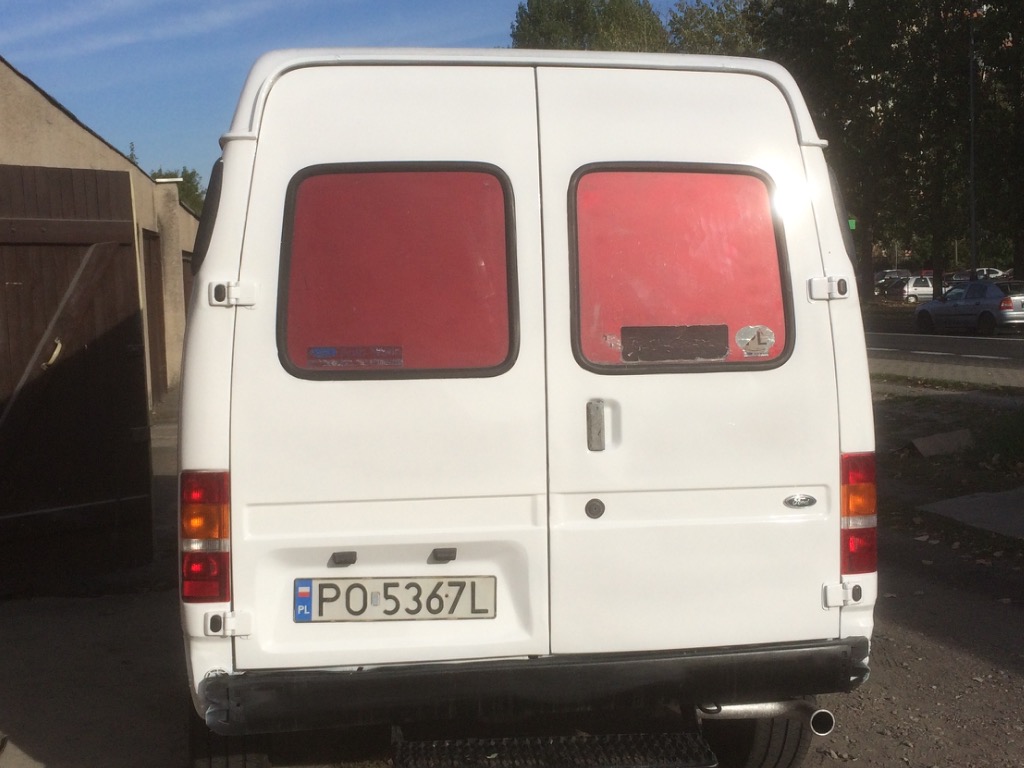 Tył białego samochodu dostawczego Ford Transit z polską tablicą rejestracyjną PO 5367L, widzianego w Czapurach, z lekko zarysowanym zderzakiem i czerwonymi szybami