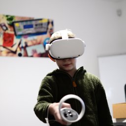 ŁOSIEM - Szkoła Języków Przyszłości - Chłopiec w okularach VR trzymający kontroler, w tle tablica i obrazek na ścianie.