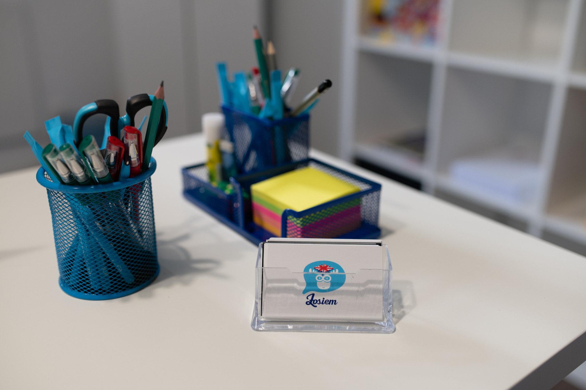 Biurko z przyborami biurowymi w odcieniach niebieskiego i wizytówkami z logo szkoły językowej z brytyjską flagą.