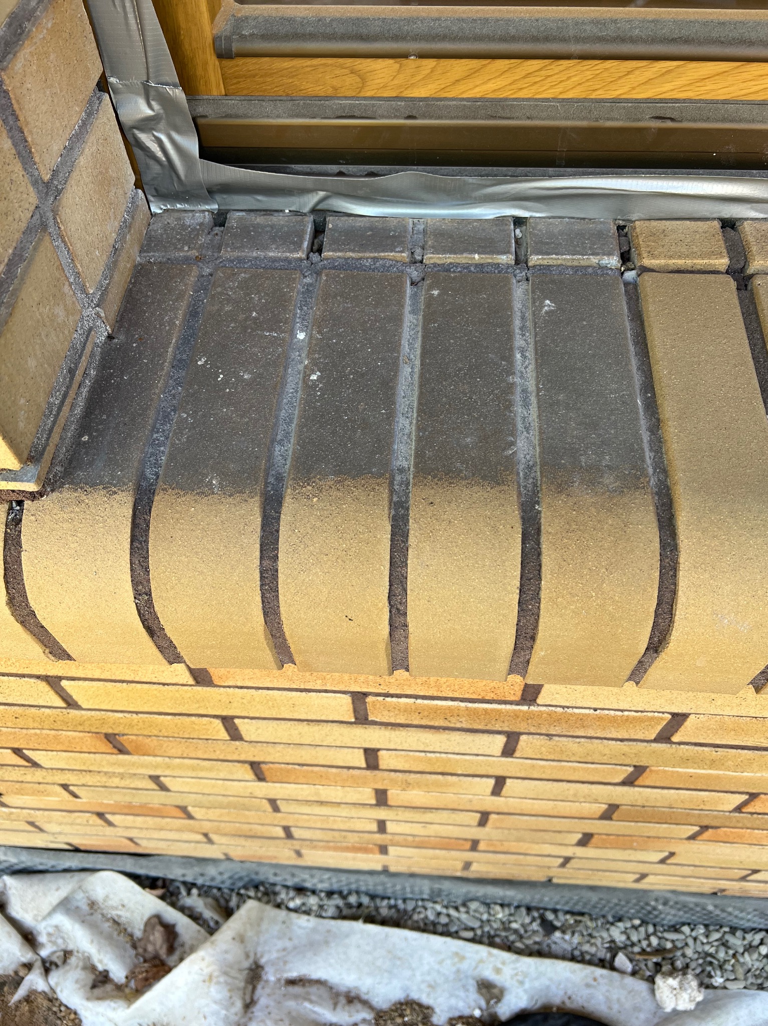 Fragment muru z cegły klinkierowej z widocznym zabrudzeniem na cokole okiennym. Ochrona okna taśmą. Detal elewacji przed czyszczeniem.