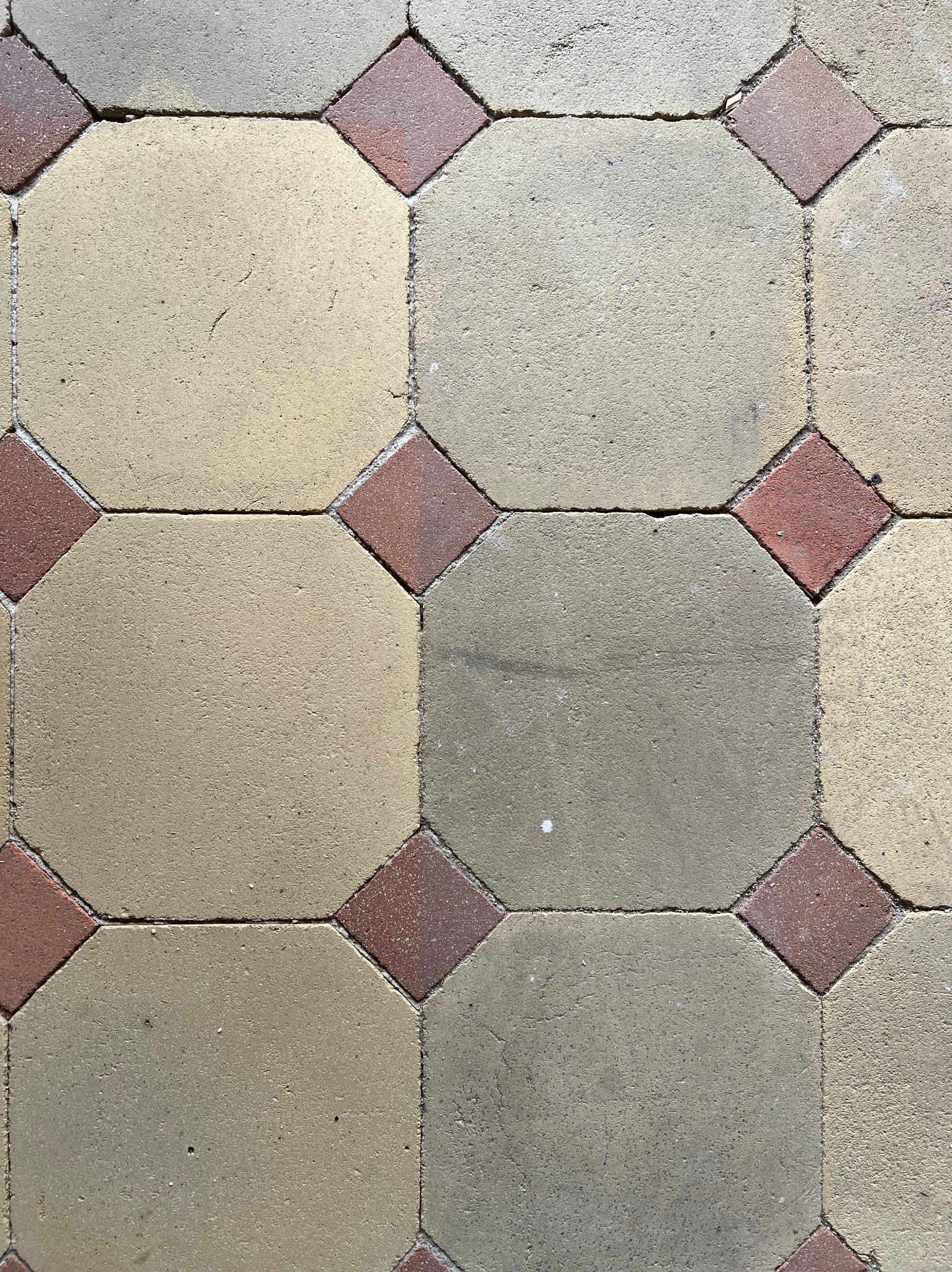 Ułożona kostka brukowa w geometryczny wzór: beżowe ośmiokąty i czerwone kwadraty. Widoczne fugi i tekstura materiału. Kąt ujęcia z góry.