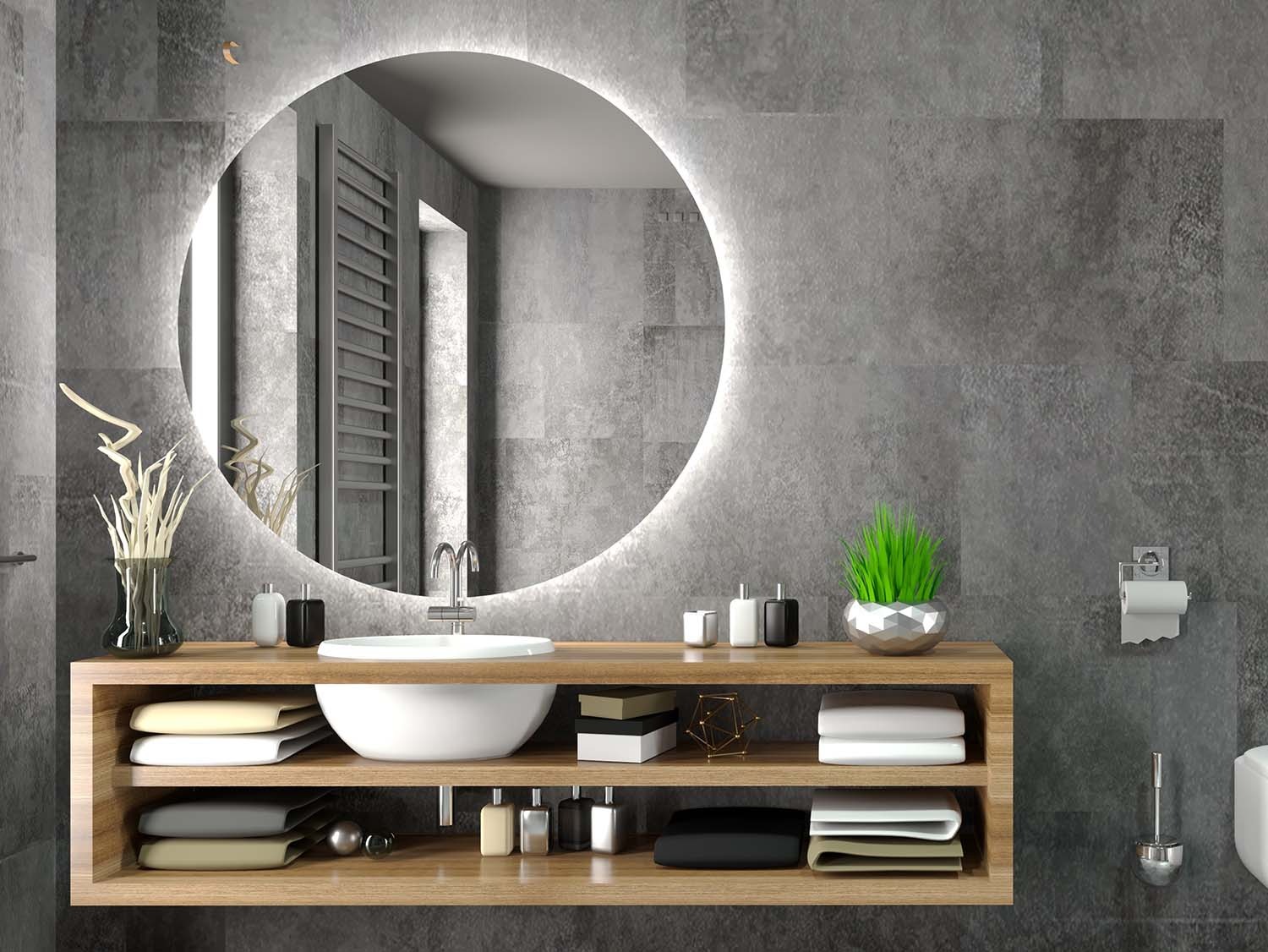 Nowoczesna łazienka z okrągłym lustrem podświetlanym LED, umywalką nablatową i drewnianą szafką wiszącą z półkami na ręczniki, na tle szarych płytek imitujących kamień.