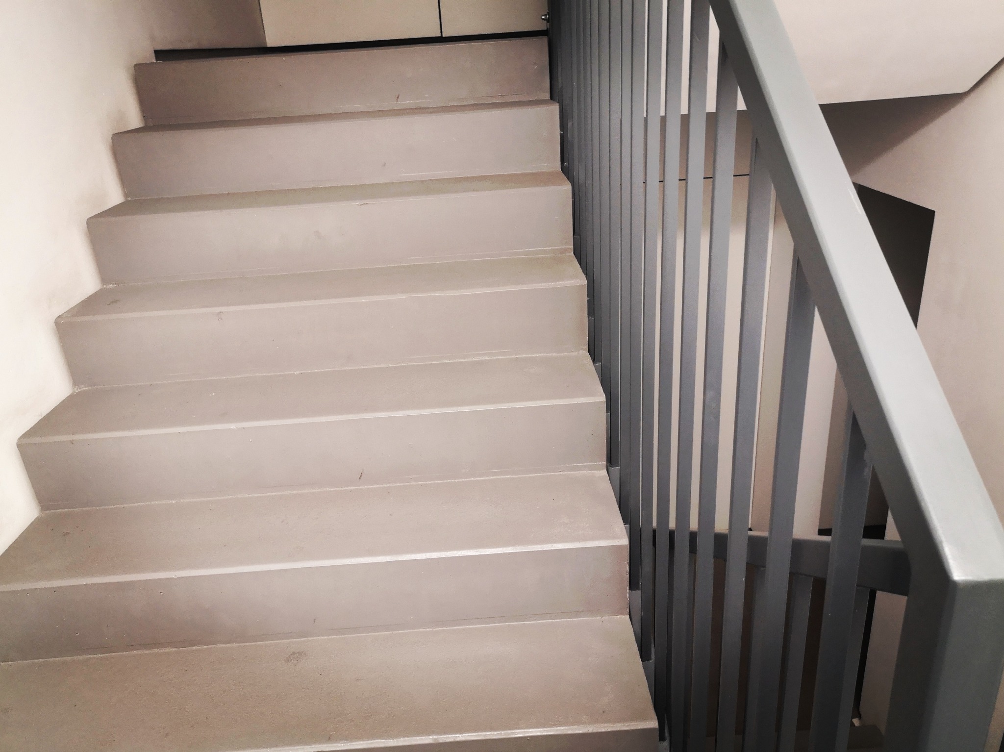 Betonowe schody z szarą metalową balustradą w klatce schodowej, widok z dołu w kierunku góry.