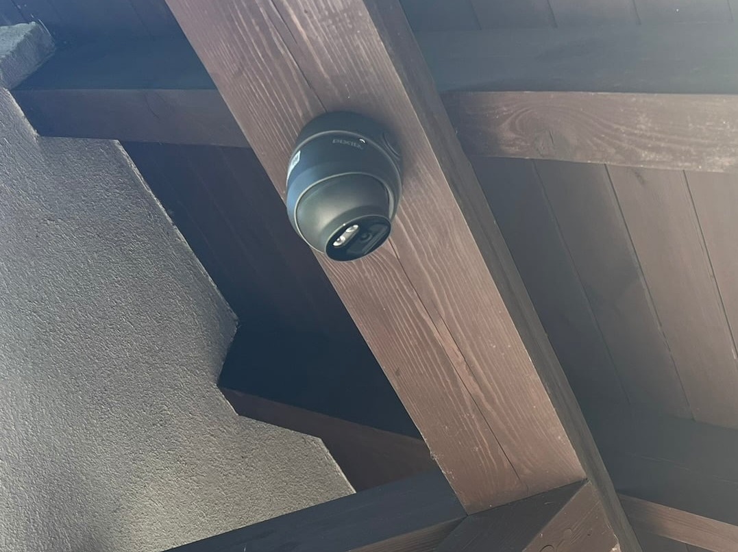 Kopułkowa kamera monitoringu marki Pixie zamontowana na drewnianej belce stropowej wewnątrz budynku, widok z dołu.
