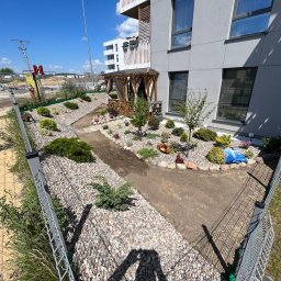 ROMBUD - Nowoczesny ogród przy apartamentowcu z drewnianą altaną, ścieżką wysypaną kamieniami, ogrodzeniem z siatki i elementami małej architektury