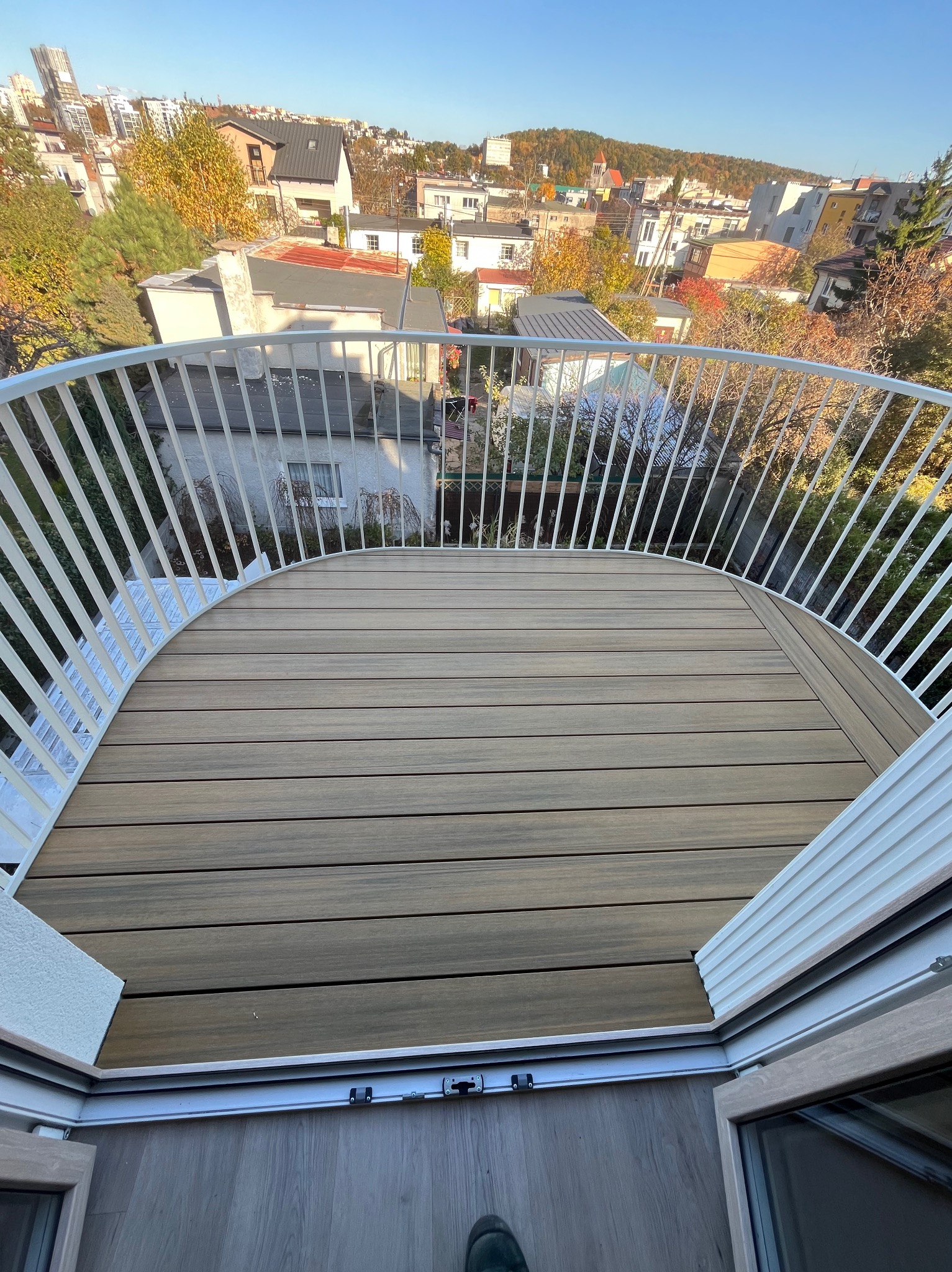 Widok z balkonu w Gdańsku z nową deską kompozytową i białymi balustradami, na tle zabudowy miejskiej i jesiennych drzew.