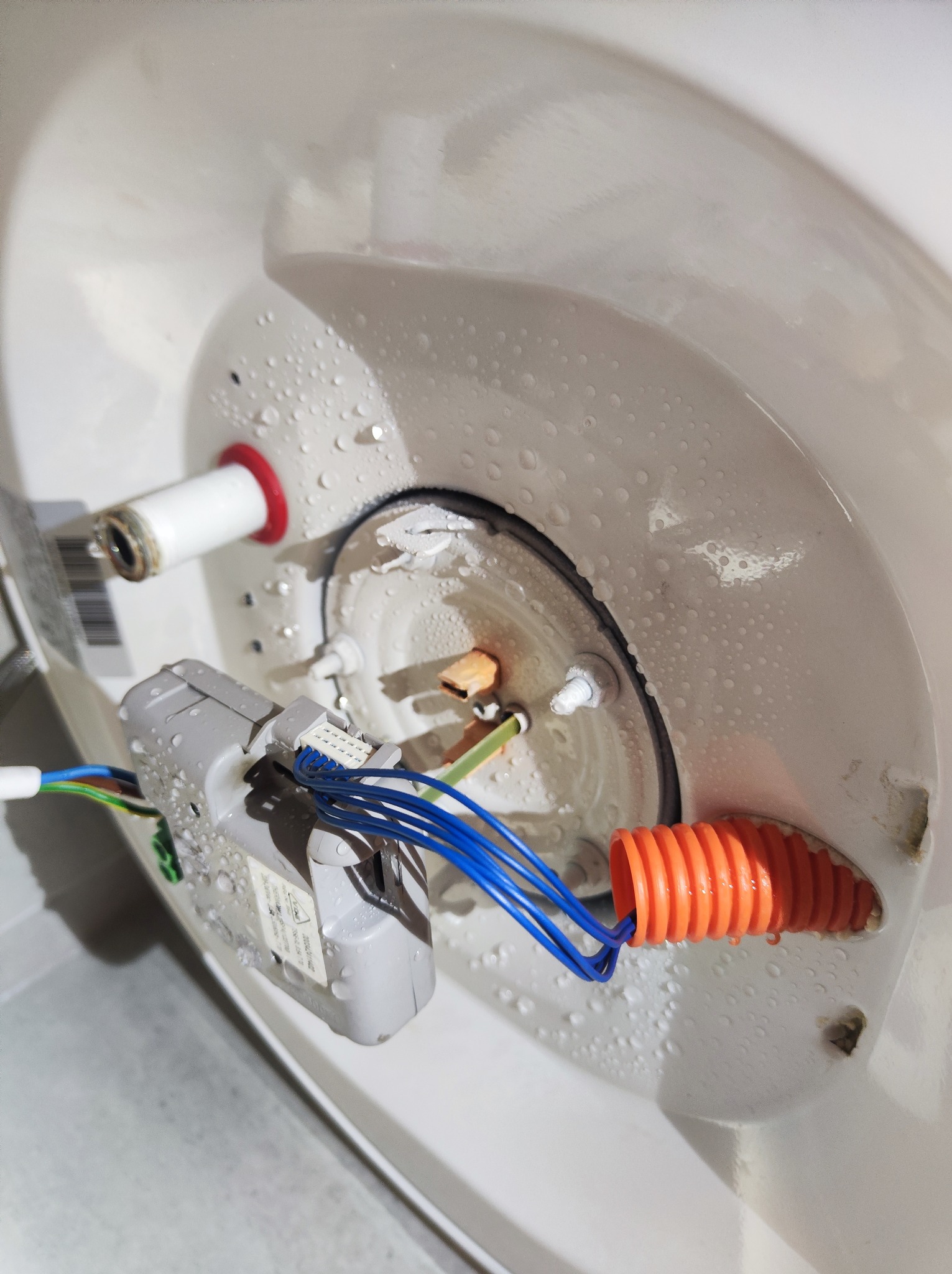 Wnętrze pieca gazowego w trakcie naprawy, widoczne elementy elektryczne, przewody i krople wody.