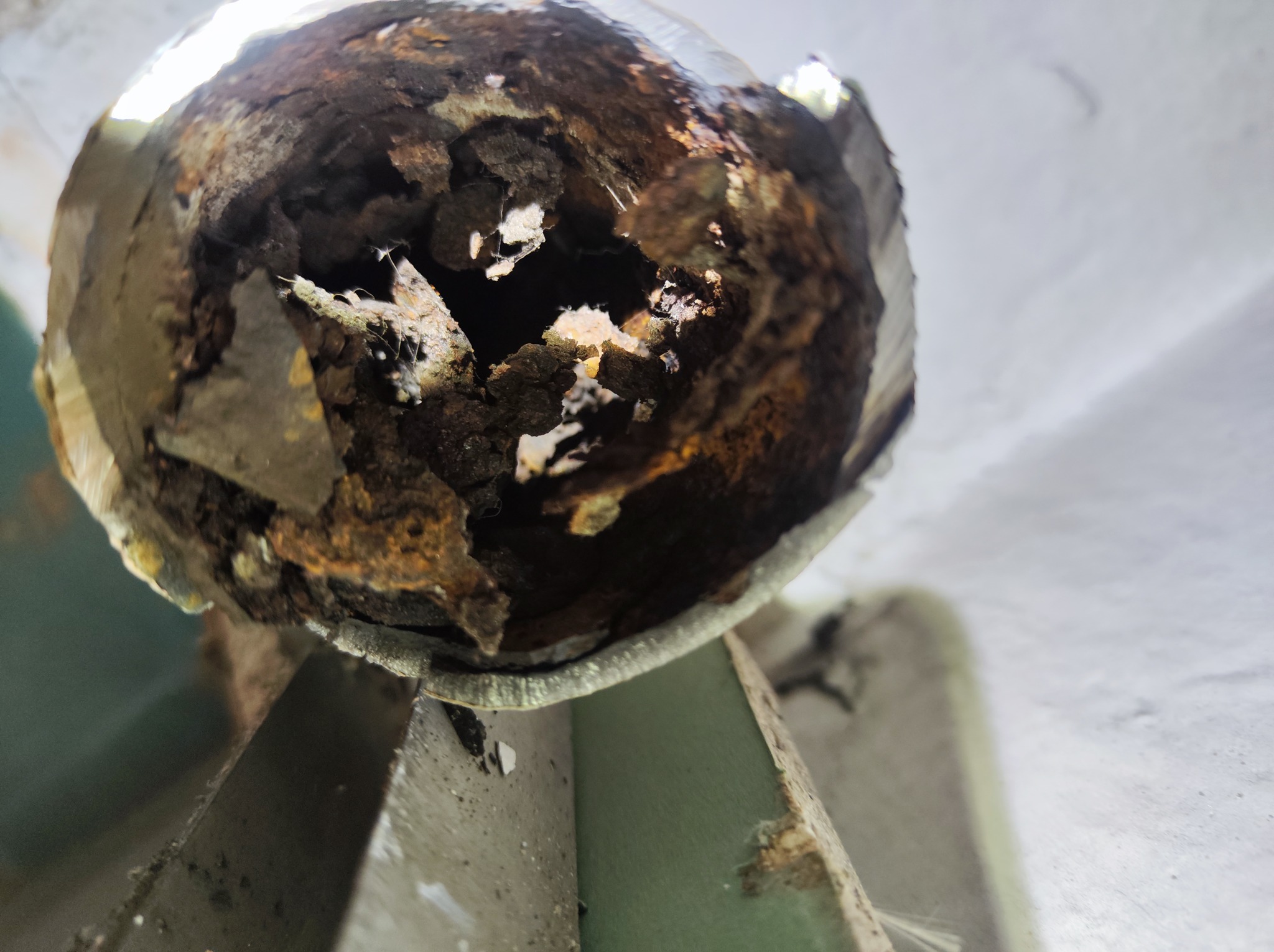 Zardzewiała, skorodowana rura hydrauliczna z widocznym wnętrzem, sfotografowana z bliska pod kątem od dołu, ukazująca stopień zniszczenia i osad.