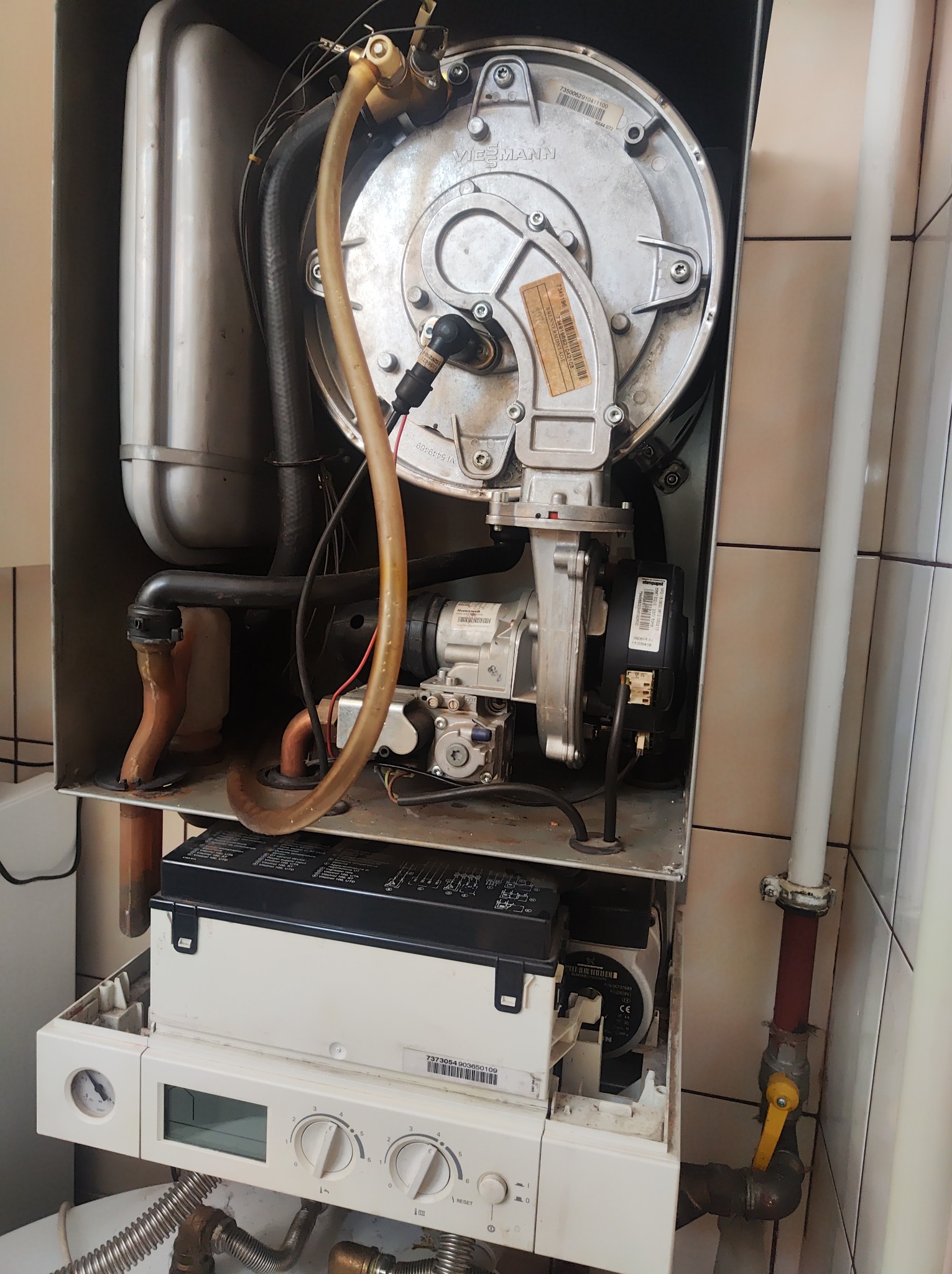 Wnętrze obudowy pieca gazowego marki Viessmann, widoczne elementy instalacji, rury miedziane i plastikowe, panel sterowania z pokrętłami, przyłącze gazowe z zaworem kulowym.