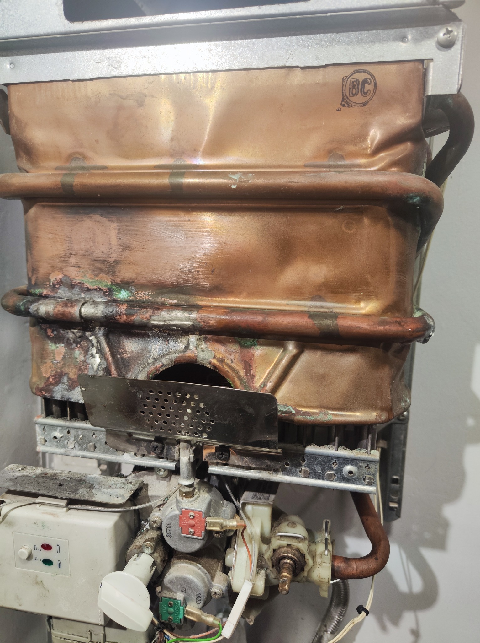 Stary, miedziany piec gazowy z widocznymi śladami użytkowania i korozji, z elementami sterującymi i rurami przyłączeniowymi.