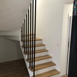 Usługi spawalnicze Mateusz Rodziewicz - Nowoczesne schody z drewnianymi stopniami i czarnymi, pionowymi elementami balustrady w jasnym wnętrzu.