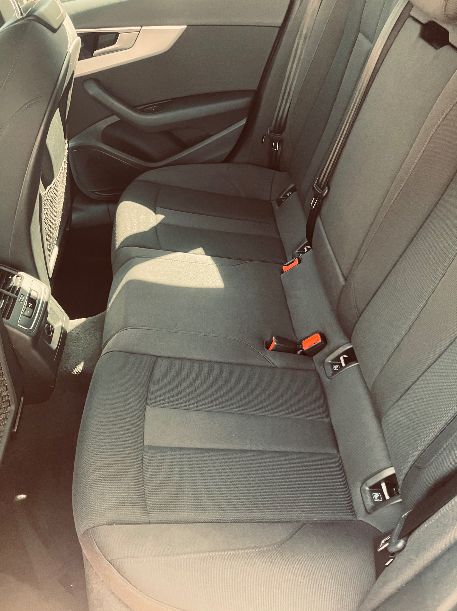 Wnętrze samochodu: tylna kanapa z szarej tapicerki z widocznymi pasami bezpieczeństwa i kratką na drobiazgi na oparciu przedniego fotela.
