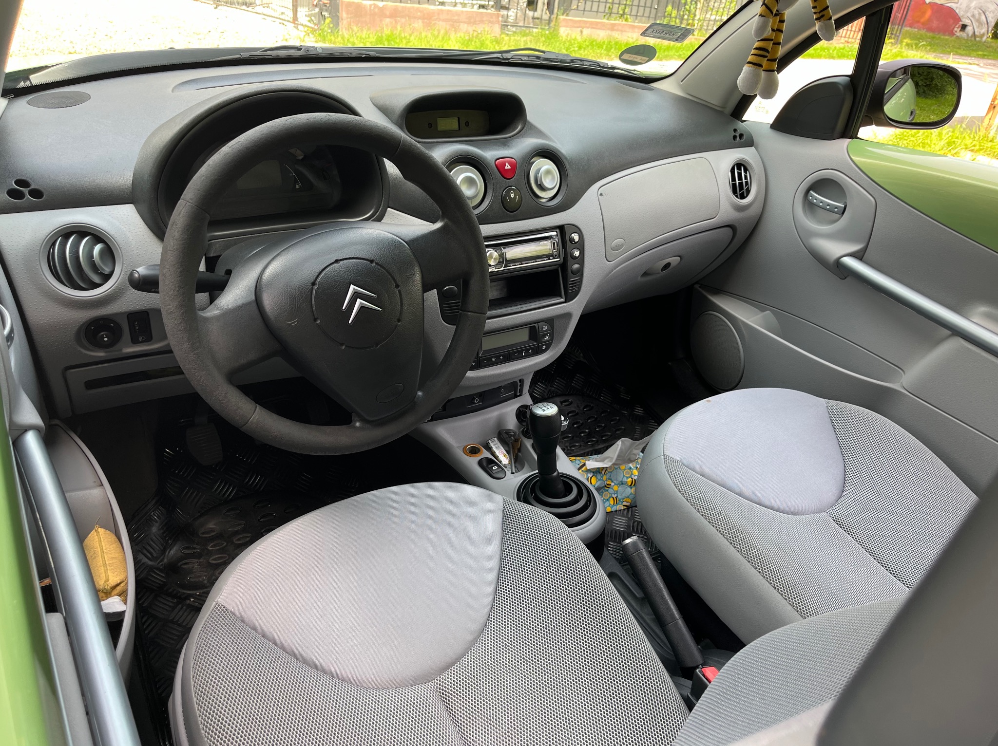 Wnętrze samochodu Citroen C3 z szarą tapicerką, widok na deskę rozdzielczą, kierownicę z logo Citroena, fotele i dźwignię zmiany biegów, dywaniki z wytłaczanym wzorem rombów.
