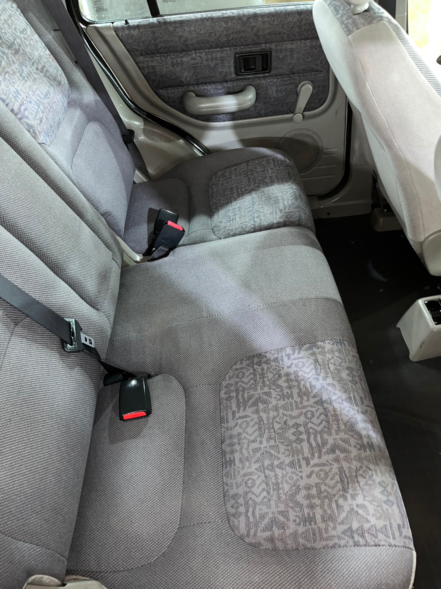 Szare tylne siedzenia samochodu z wzorzystymi wstawkami i czarnymi pasami bezpieczeństwa.