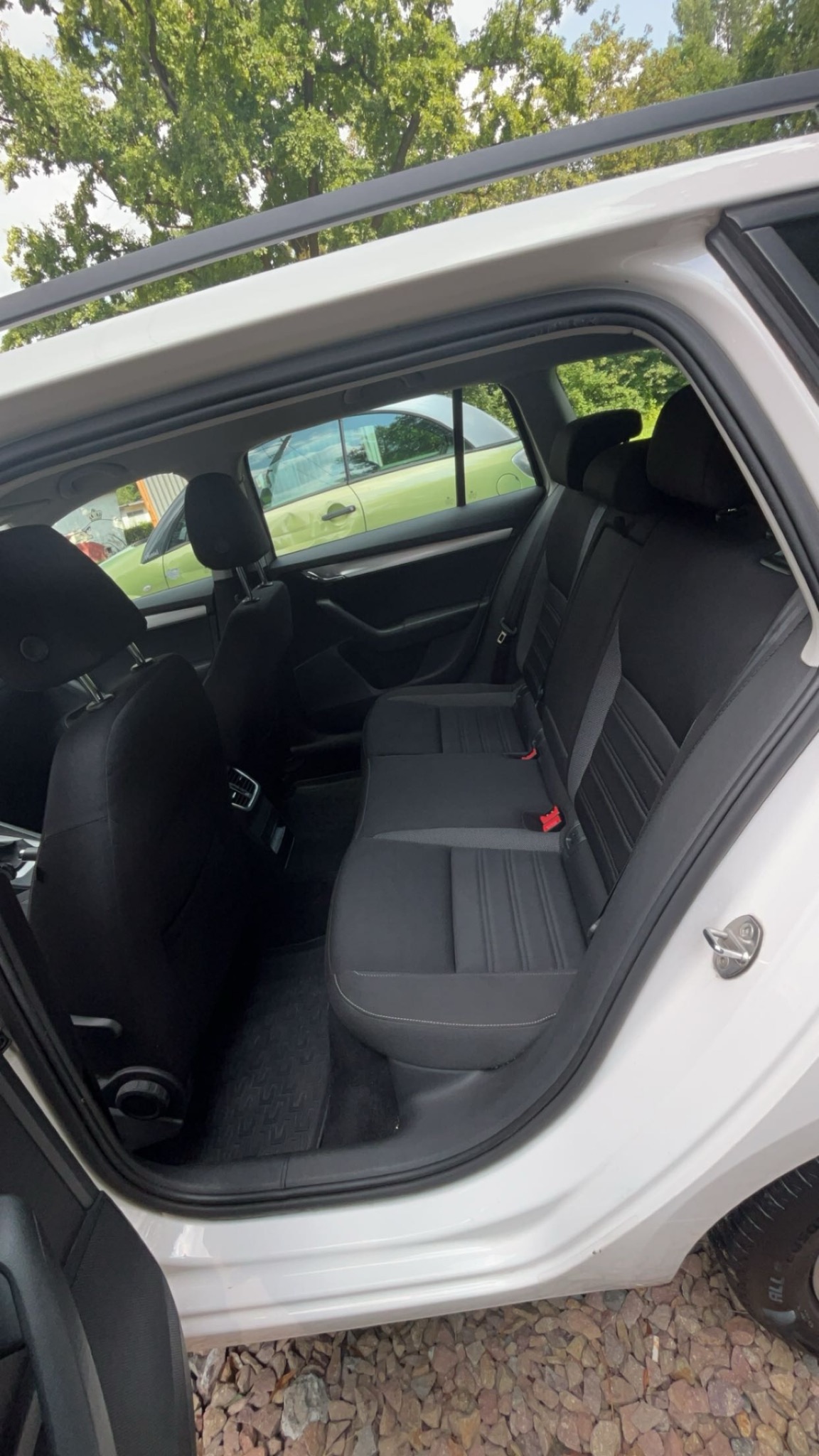 Wnętrze białego samochodu kombi z czarną tapicerką, widok z otwartych drzwi, na zewnątrz widoczny zielony samochód.