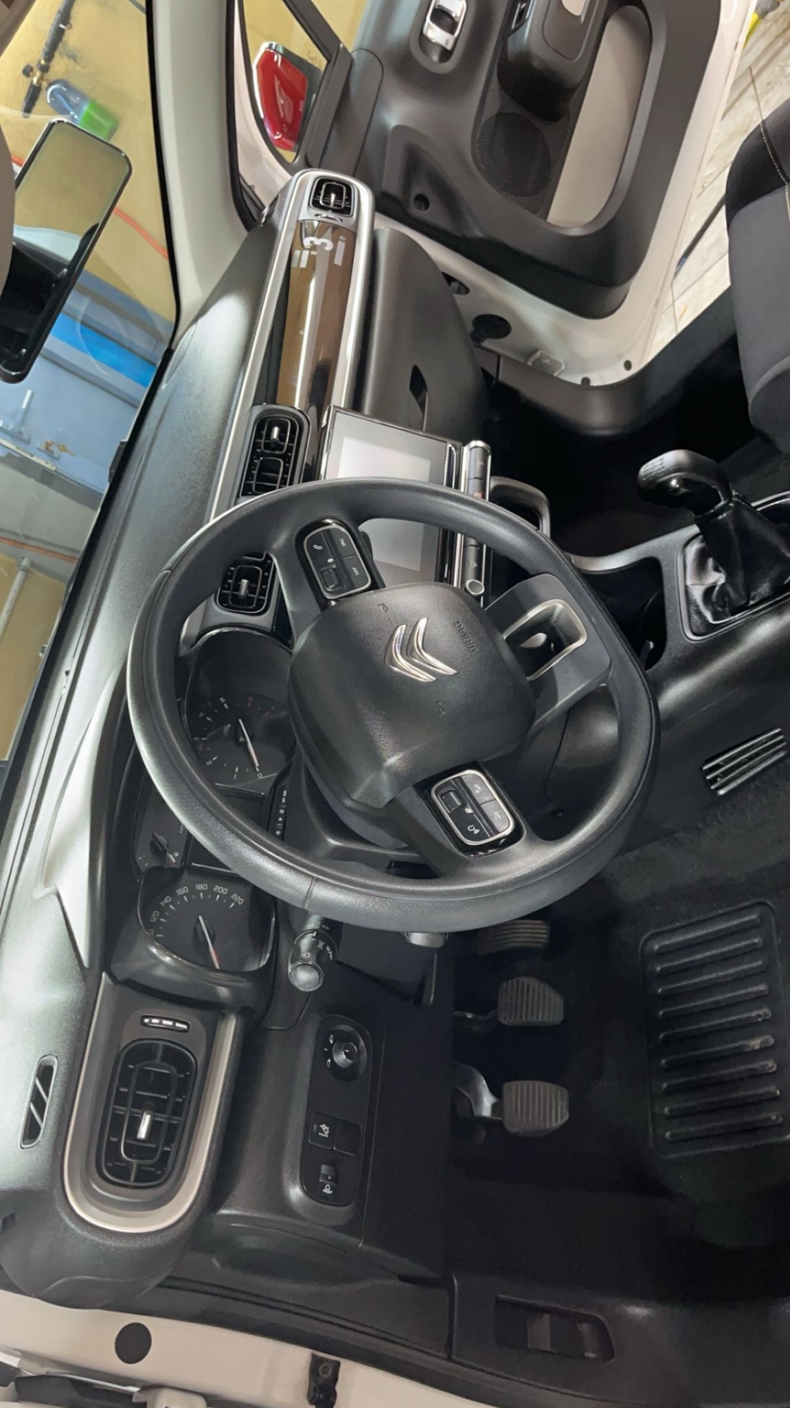 Wnętrze samochodu marki Citroën, widok na deskę rozdzielczą, kierownicę z logo, pedały i fragment fotela, ukazujące czystość i zadbane detale.