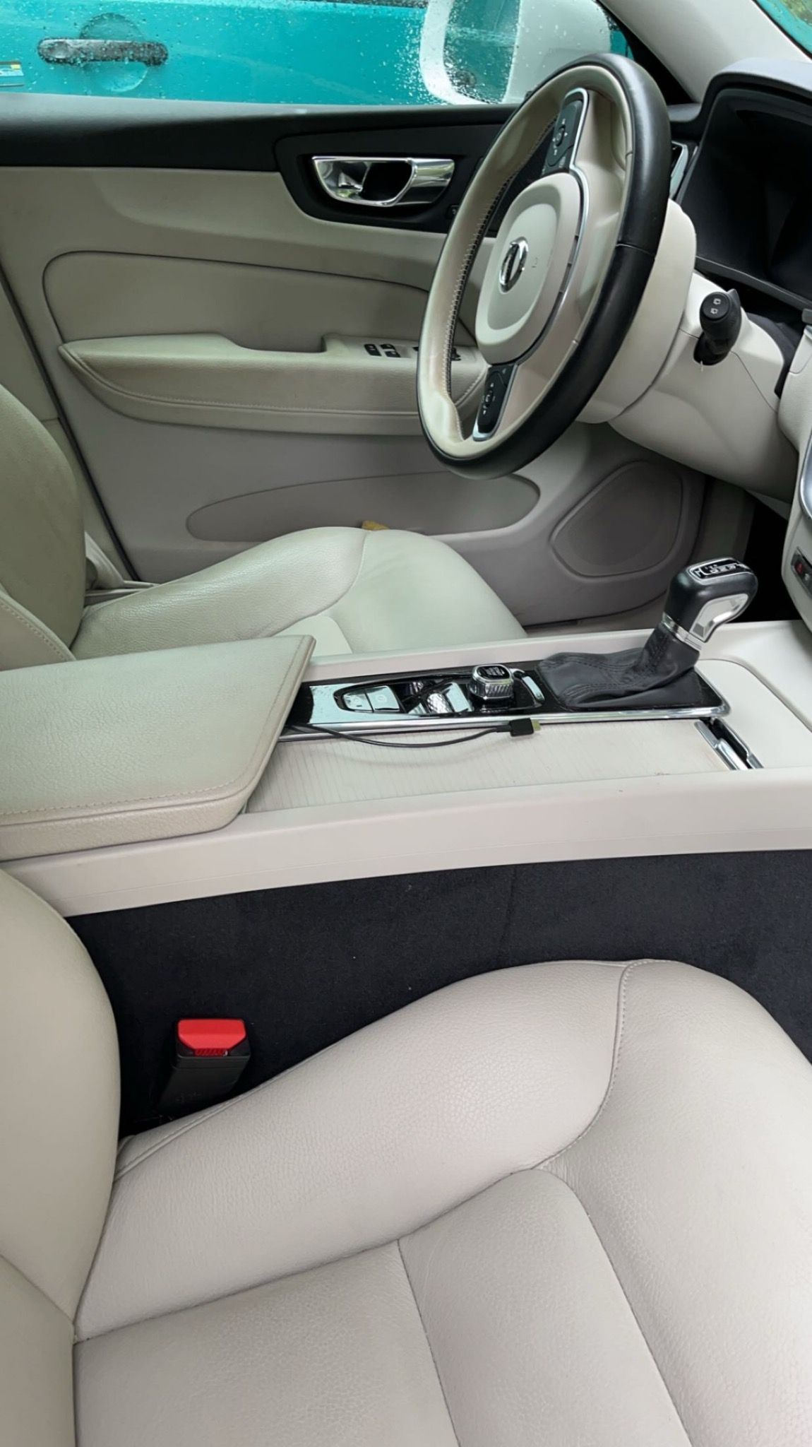 Jasne, skórzane wnętrze samochodu Volvo, widok na kierownicę, deskę rozdzielczą i fotele z perspektywy pasażera.