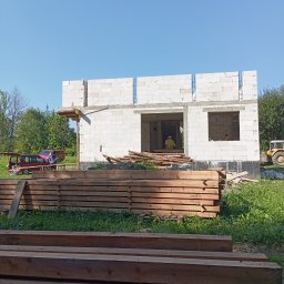 J3crewbau - Wznoszenie ścian parterowego domu z betonu komórkowego. Widoczne drewniane elementy konstrukcyjne, materiały budowlane i pracownicy w środku budynku.