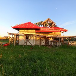 J3crewbau - Niedokończony dom z czerwonym dachem i drewnianą konstrukcją, otoczony zielonym polem, w tle błękitne niebo z widocznym księżycem. Etap budowy.