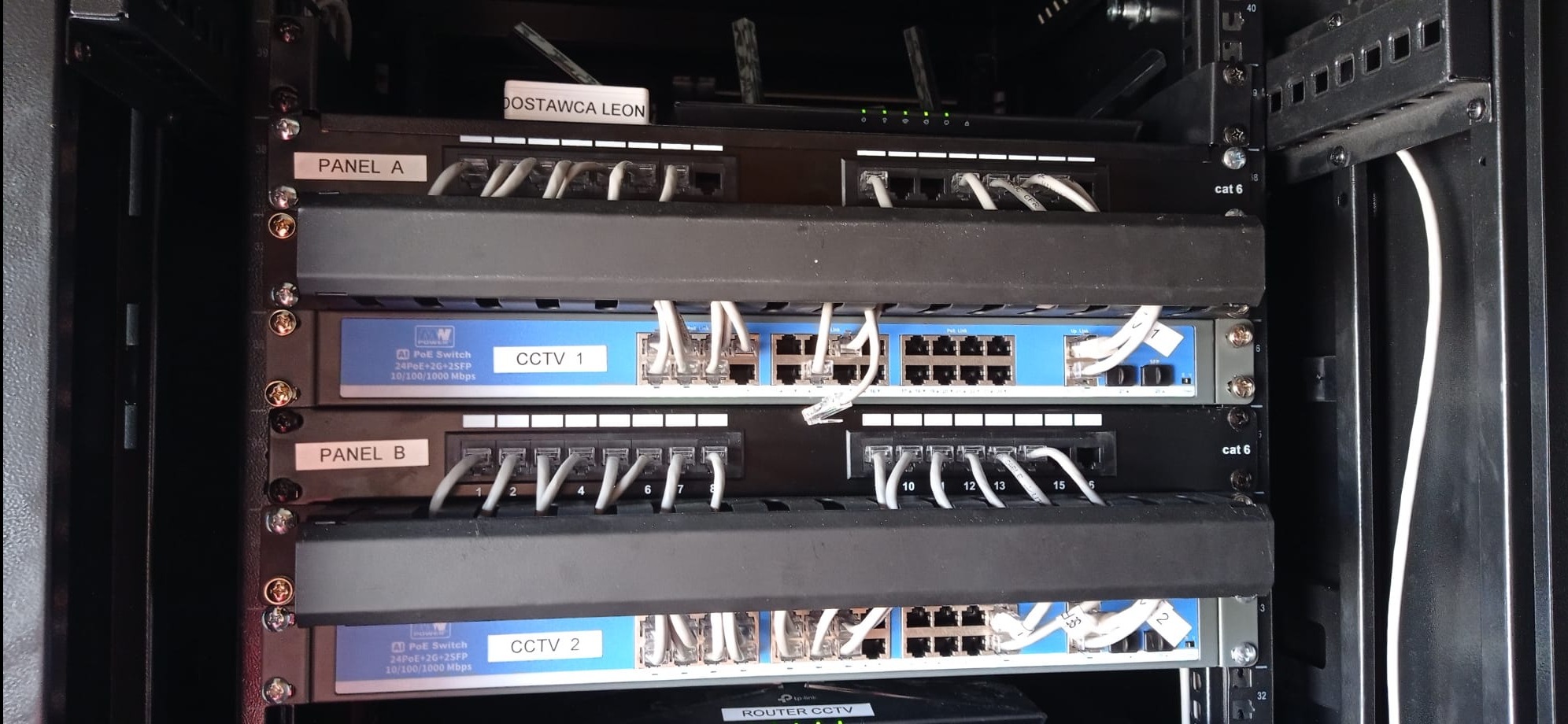 Szafa rack z panelami krosowniczymi i przełącznikami PoE, okablowanie sieciowe, etykiety 'CCTV 1' i 'CCTV 2' na przełącznikach, router CCTV na dole szafy.