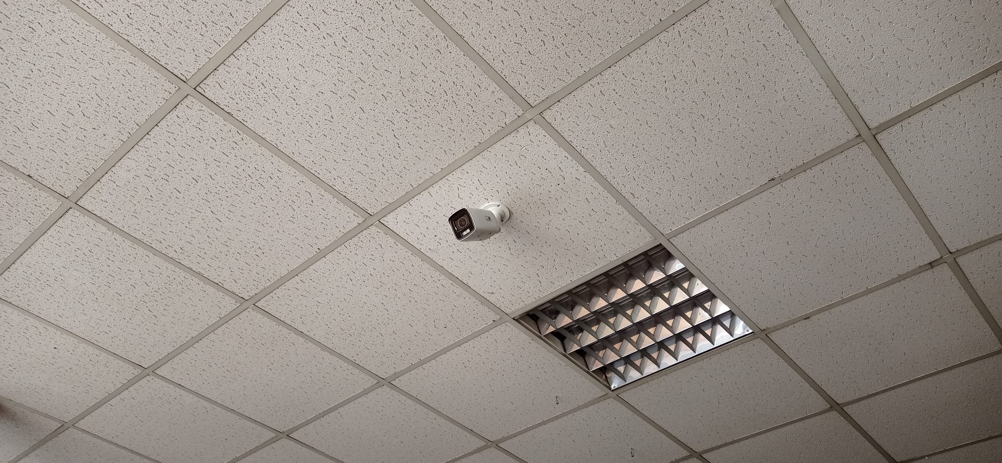 Kamera monitoringu zamontowana na suficie podwieszanym z kasetonów w Raciborzu, obok oprawy oświetleniowej rastrowej.