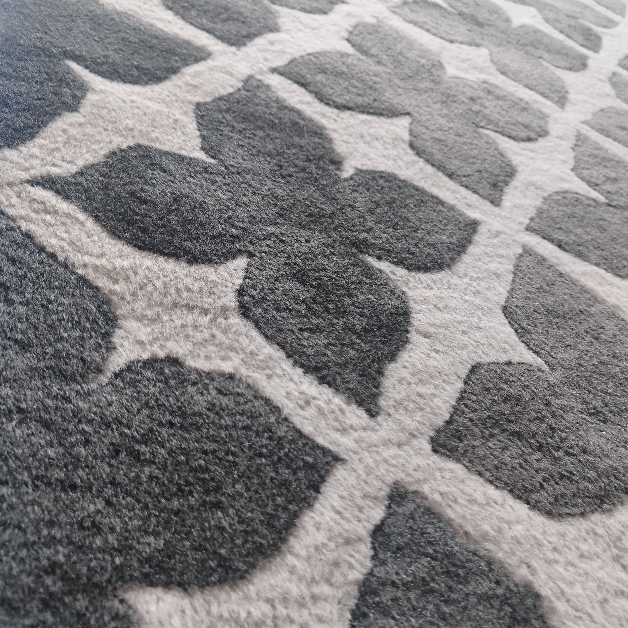 Szczegółowy widok szarego dywanu z wzorem w kształcie liści na kremowym tle, ukazujący strukturę włókien i fakturę materiału.