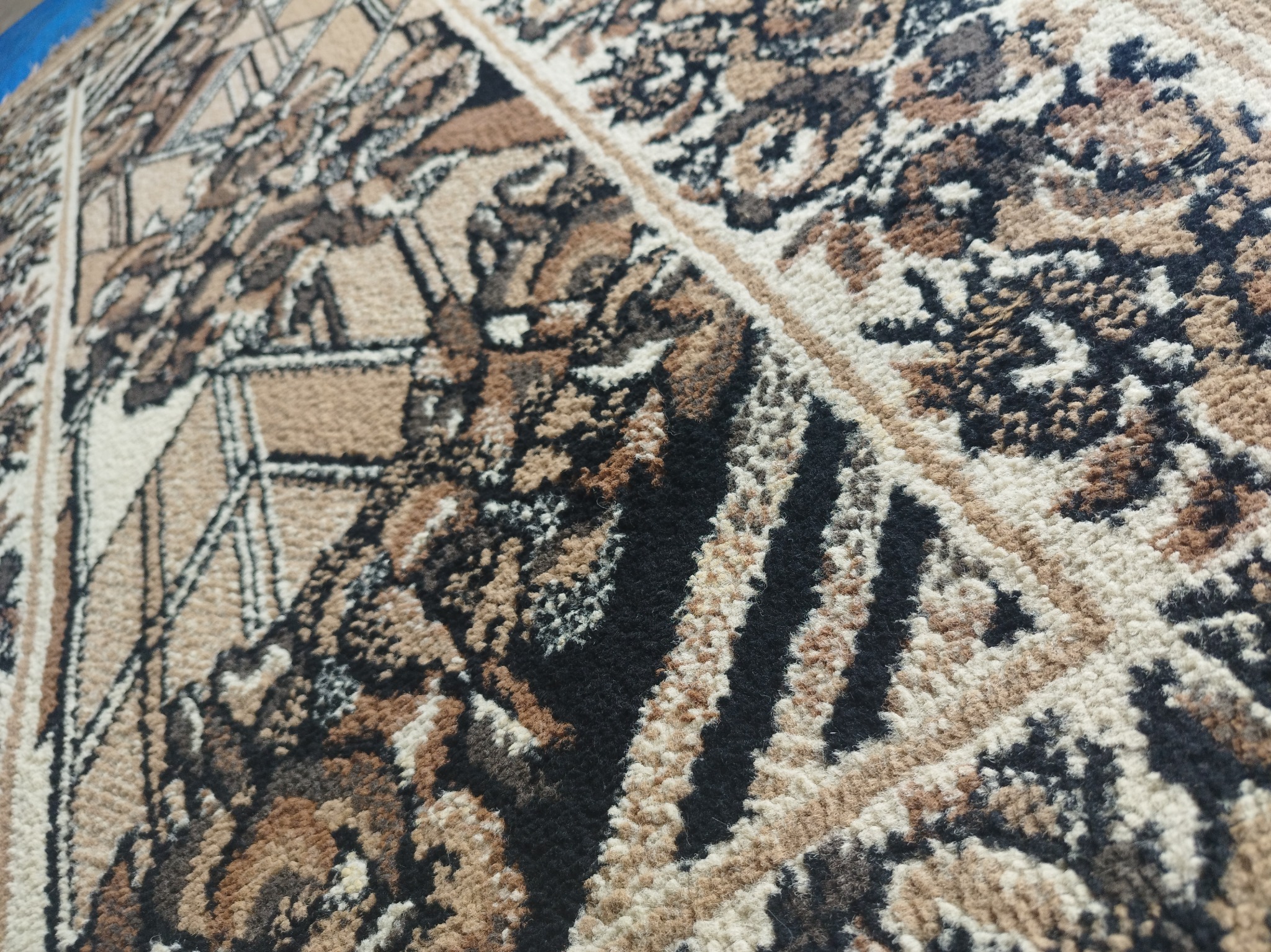 Fragment wzorzystego dywanu w odcieniach brązu, beżu i czerni, z wyraźną fakturą włókien i podziałem na sekcje.