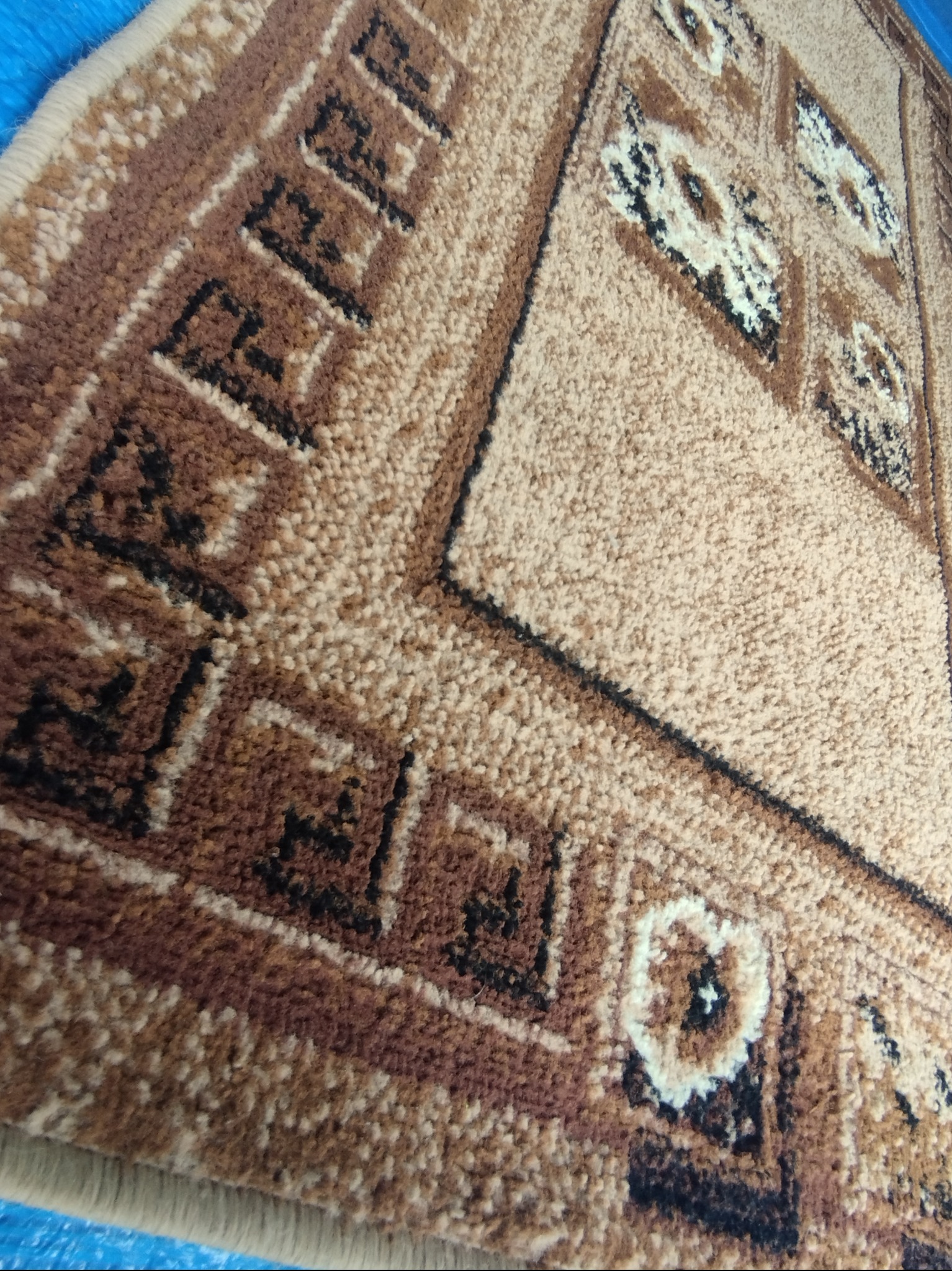 Fragment brązowego dywanu z geometrycznym wzorem i kwiatowymi motywami, widoczny z bliska pod kątem.