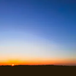 Horyzont z zachodzącym słońcem, ciemny pas drzew na tle pomarańczowo-niebieskiego nieba.