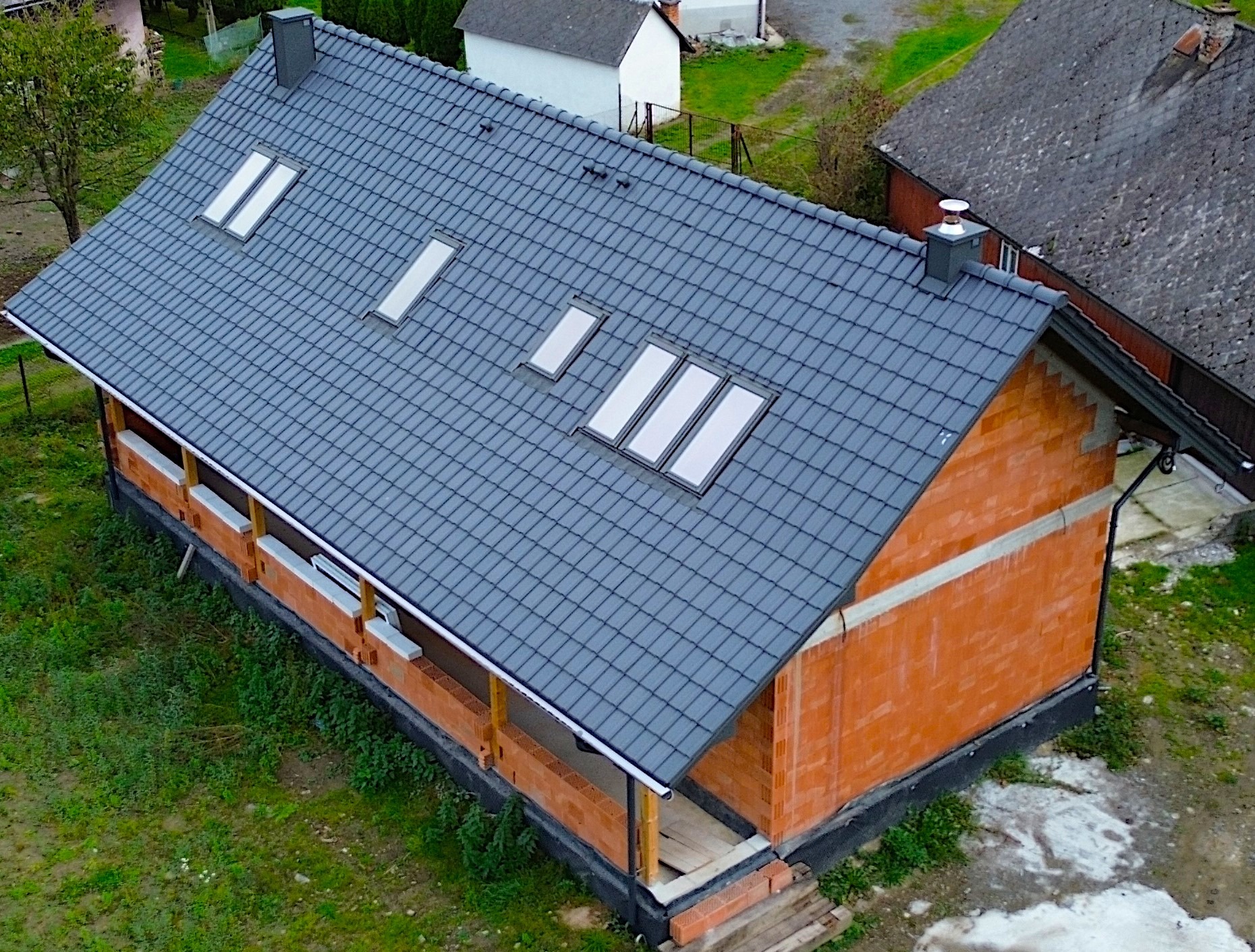 Niedokończony dom z czerwonej cegły z ciemnoszarym dachem z dachówkami i trzema oknami dachowymi, widok z góry.