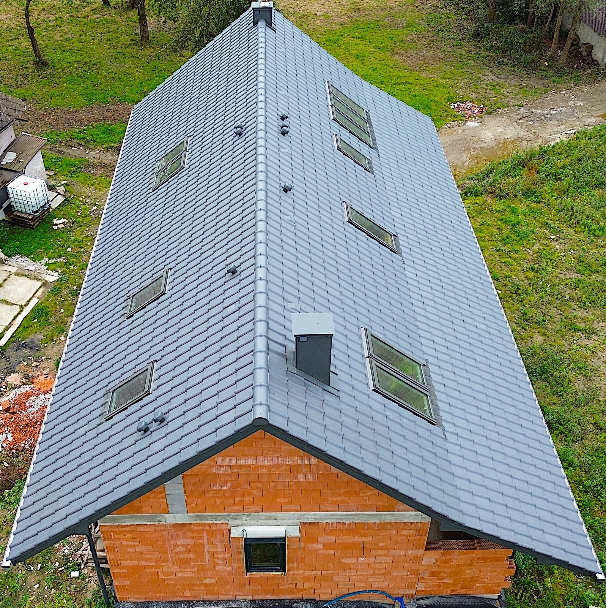 Widok z góry na szary dach z dachówką ceramiczną z oknami dachowymi i kominem na domu w trakcie budowy z czerwonej cegły.