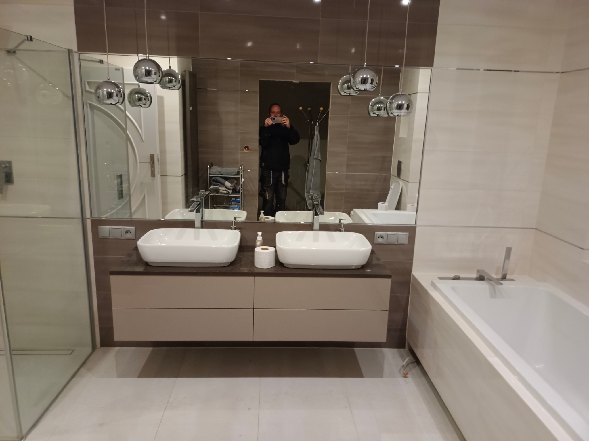 Nowoczesna łazienka z dwoma umywalkami nablatowymi, dużym lustrem i wiszącymi lampami kulami, widok odbicia fotografa w lustrze.