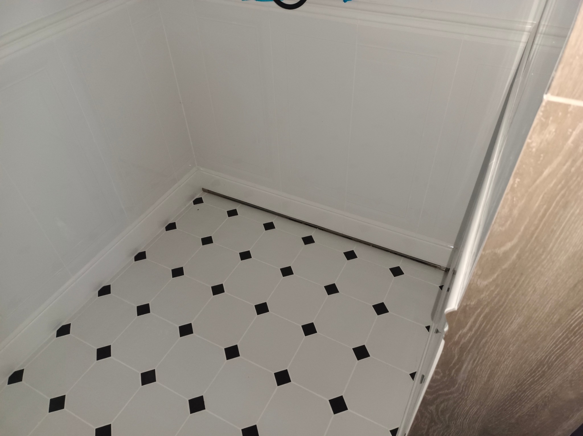 Biała kabina prysznicowa z panelami ściennymi i podłogą w biało-czarną szachownicę, widok z góry.