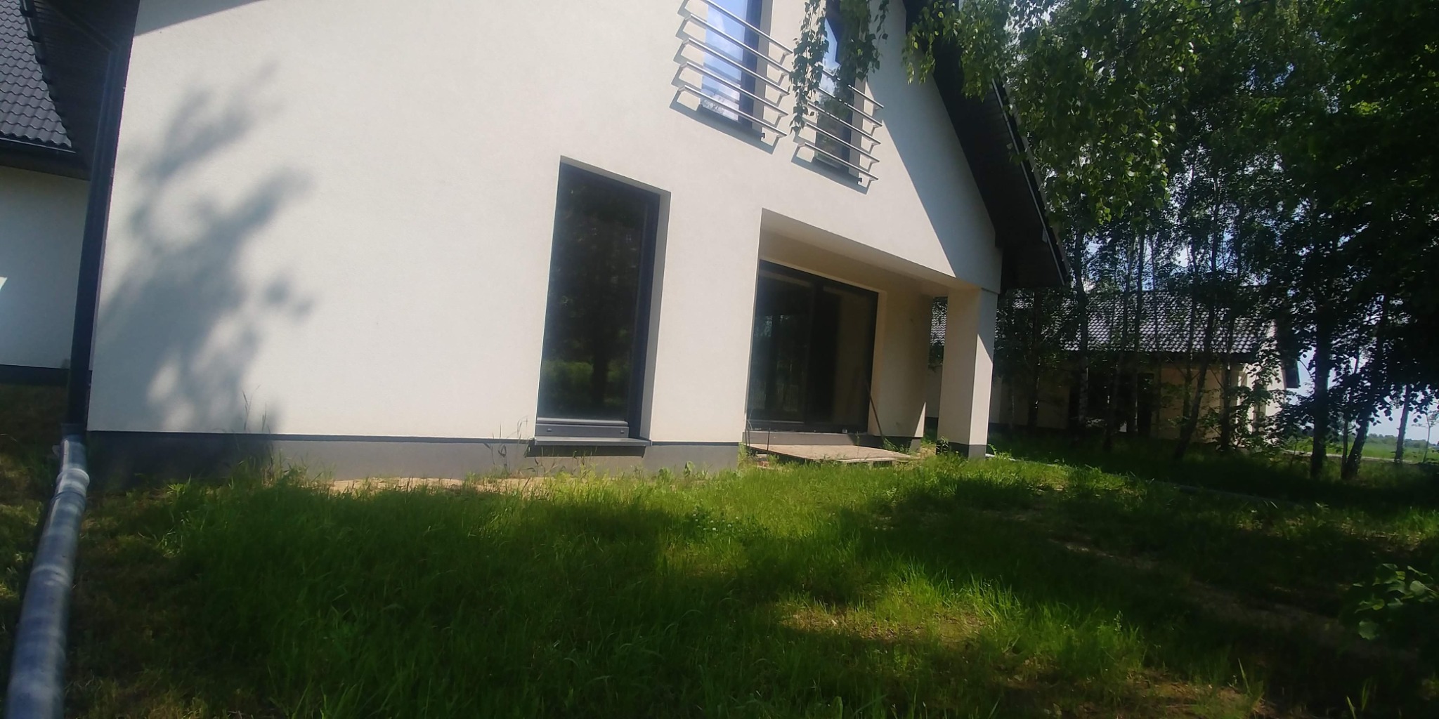 Elewacja domu z białym tynkiem, dużymi oknami i metalową balustradą, widok z poziomu trawnika