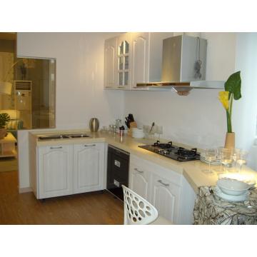 Jasna kuchnia w stylu prowansalskim z białymi szafkami, blatem z jasnego kamienia i sprzętami AGD ze stali nierdzewnej. Widoczne naczynia i dekoracje na blacie, w tle salon.