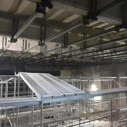 Usługi remontowo-budowlane Marcin Jakoniuk - Wnętrze w trakcie prac remontowych z widocznymi rusztowaniami, stalowymi belkami pod sufitem i elementami konstrukcyjnymi w surowym stanie.