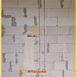 Srokowski Instalacje elektryczne - Ściana z betonu komórkowego z poprowadzonymi przewodami elektrycznymi w peszlach i puszkami instalacyjnymi. Widoczne drewniane elementy konstrukcji dachu.