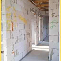 Srokowski Instalacje elektryczne - Instalacja elektryczna w surowym budynku z białego bloczka: kable prowadzone po ścianach i pod sufitem, widoczne puszki instalacyjne. Etap prac przed tynkowaniem.