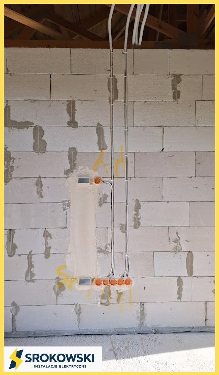 Ściana z betonu komórkowego z poprowadzonymi przewodami elektrycznymi w peszlach i puszkami instalacyjnymi. Widoczne drewniane elementy konstrukcji dachu.