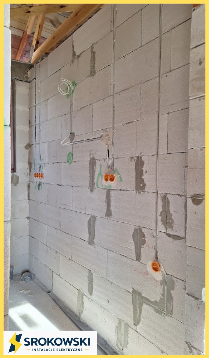 Ściana z betonu komórkowego z widoczną instalacją elektryczną: kable w peszlach, puszki pod gniazdka i włączniki, okablowanie pod oświetlenie. Surowy stan, w trakcie prac.