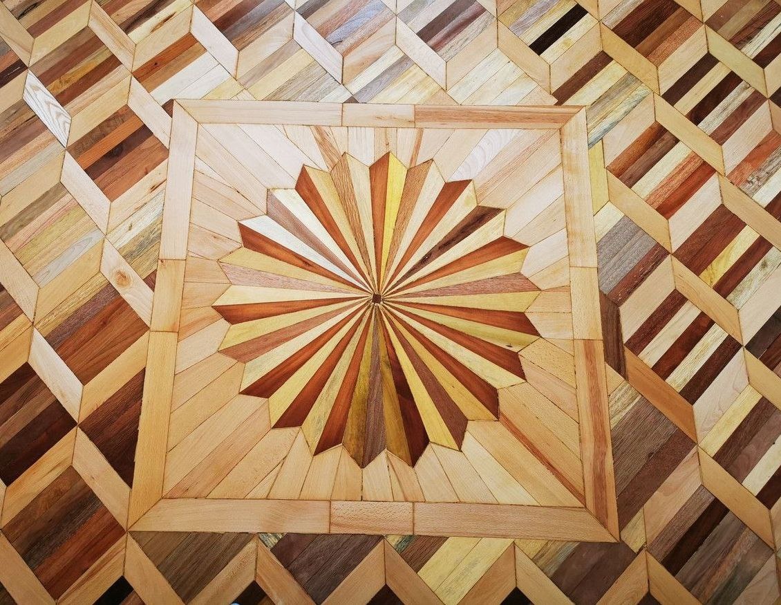 Dekoracyjna podłoga z parkietu ułożona we wzór rozety i rombów, z wykorzystaniem różnych odcieni drewna, widok z góry.
