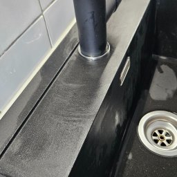 SPRZĄTANIE NIERUCHOMOŚCI MAŁGORZATA KUFERA - Czarny, granitowy zlew z czarną baterią po czyszczeniu, widoczne ślady polerowania powierzchni.