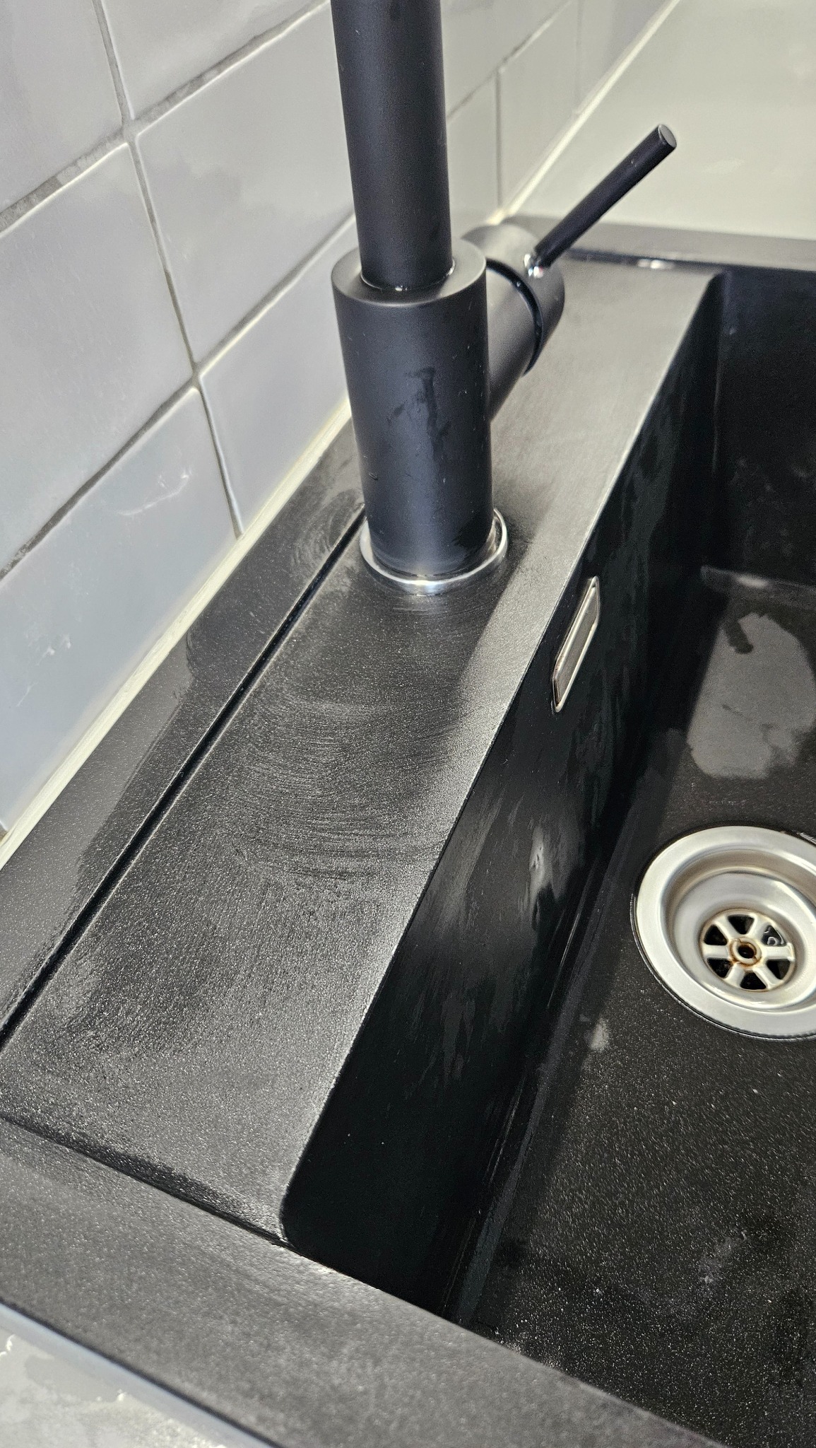 Czarny, granitowy zlew z czarną baterią po czyszczeniu, widoczne ślady polerowania powierzchni.