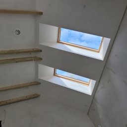 MARBUD - Wnętrze w trakcie prac wykończeniowych, widok na sufit z dwoma oknami dachowymi i drewnianymi elementami konstrukcyjnymi, ślady po wstępnym wyrównywaniu powierzchni.