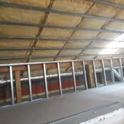 Konstrukcja metalowa ścianki działowej na poddaszu, widoczna izolacja stropu wełną mineralną i fragment instalacji wentylacyjnej.