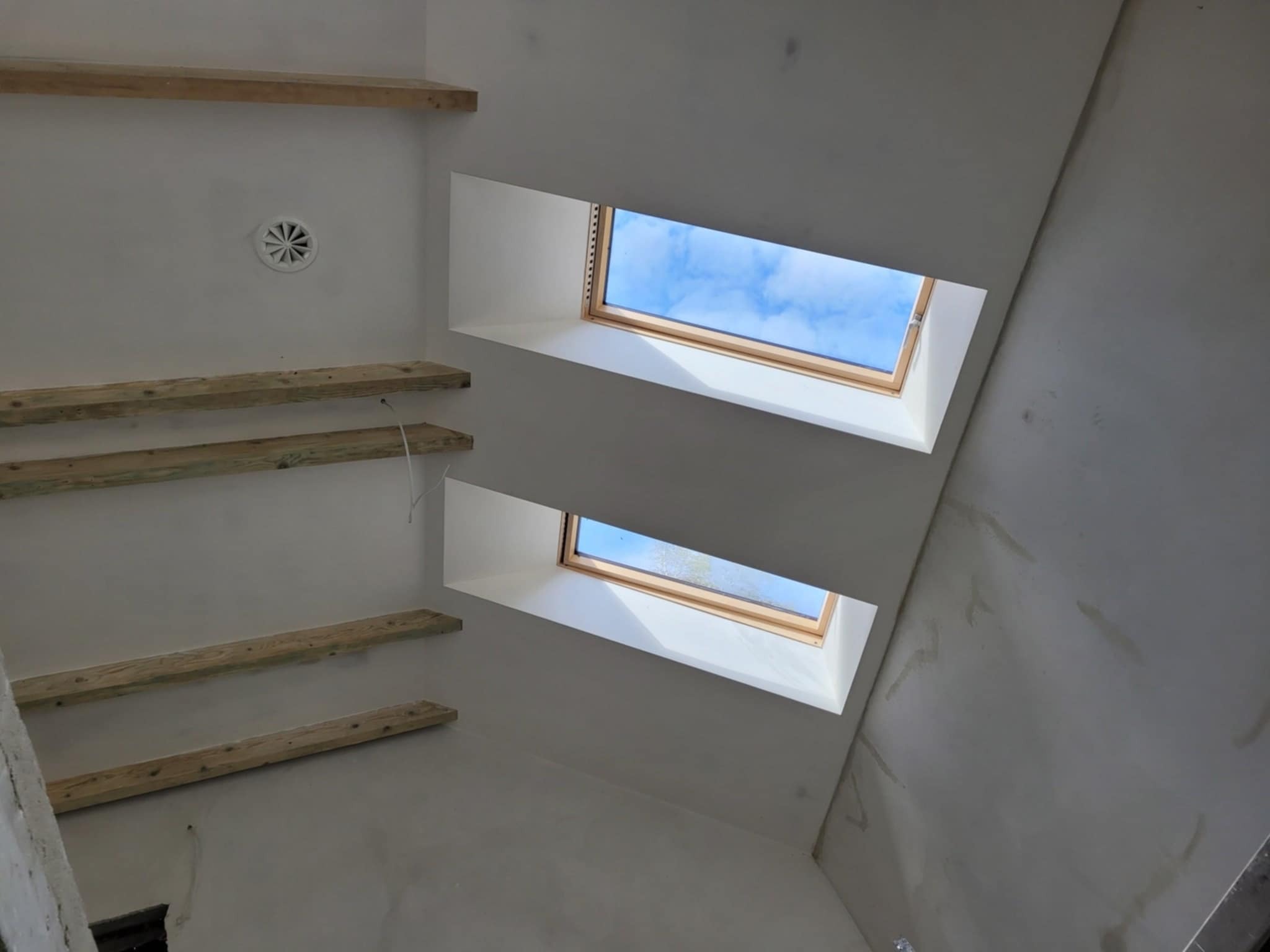 Wnętrze w trakcie prac wykończeniowych, widok na sufit z dwoma oknami dachowymi i drewnianymi elementami konstrukcyjnymi, ślady po wstępnym wyrównywaniu powierzchni.